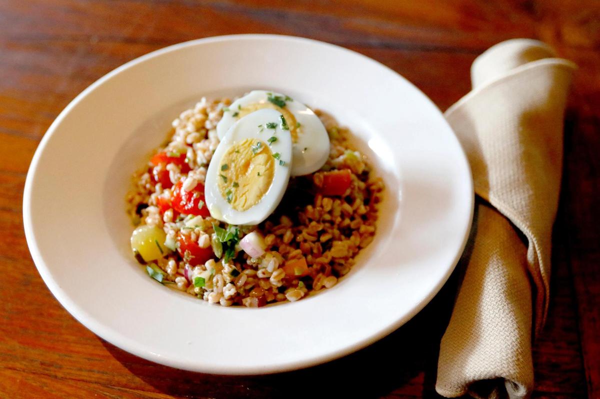 Farro Salad is made with olives, cherry tomatoes, red onion, celery, cucumber, topped with a hard boiled egg and the house dressing.