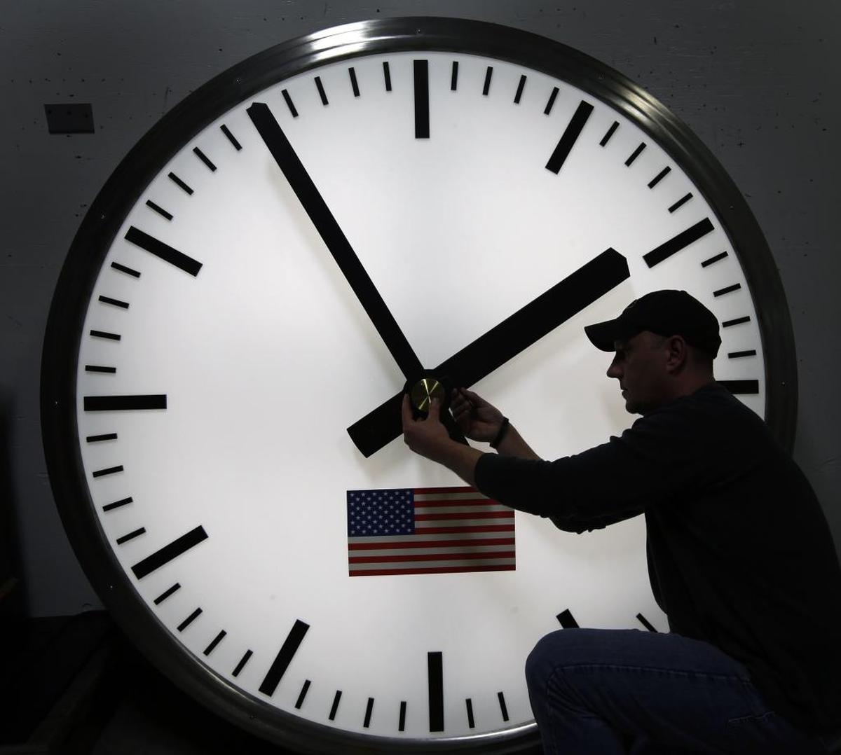A worker uses an allen wrench to adjust hands on a stainless steel tower clock in Medfield, Mass., on March 7, 2014 file photo.