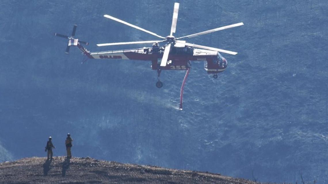 A Skycrane helitanker passes firefighters atop a hillside while coming in for a water drop below East Camino Cielo.