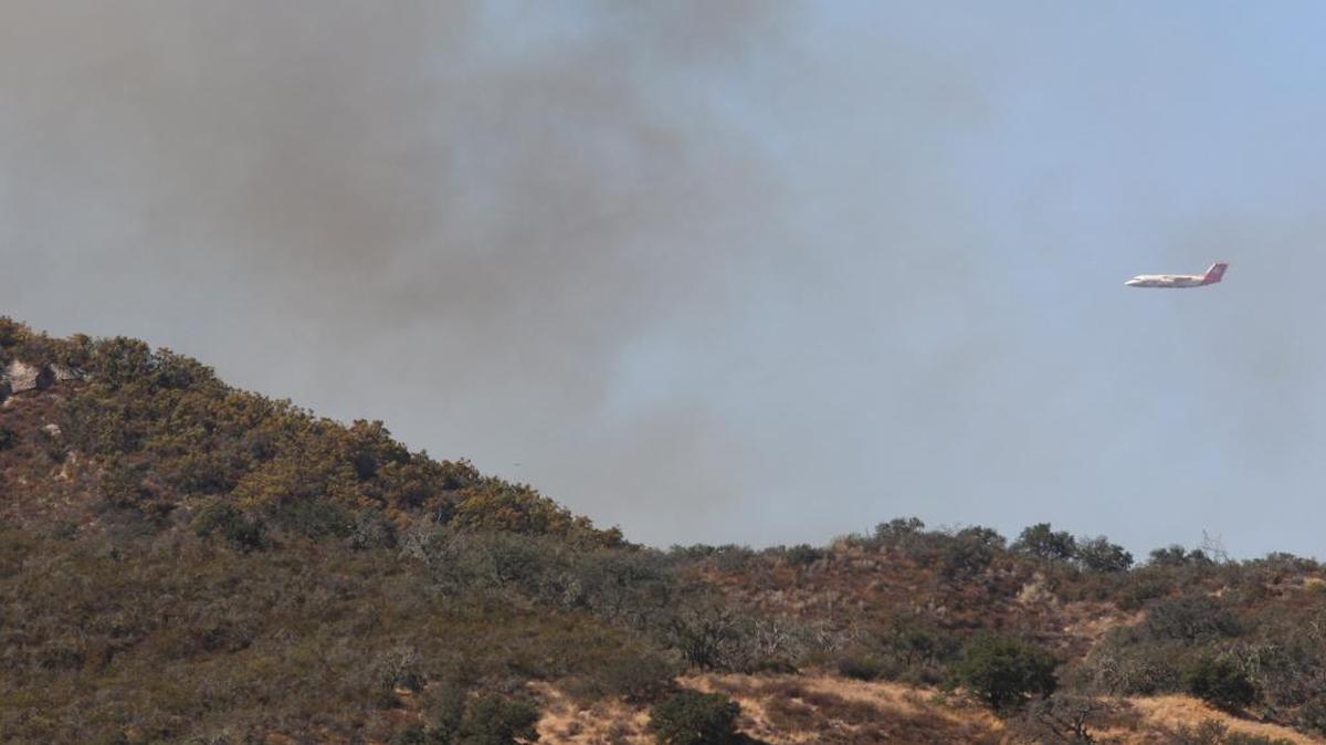 Firefighters worked in the steep hills near Huasna east of Arroyo Grande on Wednesday afternoon. An air tanker approaches for a drop.