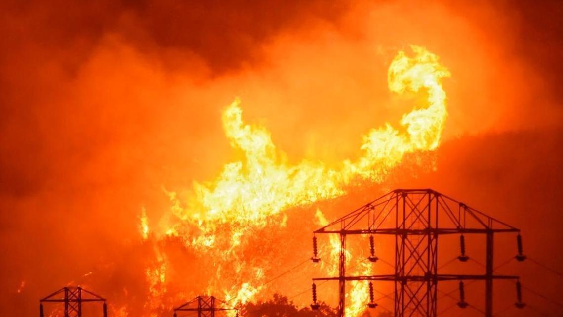 In this Saturday, Dec. 16, 2017, photo provided by the Santa Barbara County Fire Department, flames burn near power lines in Sycamore Canyon near West Mountain Drive in Montecito, Calif.