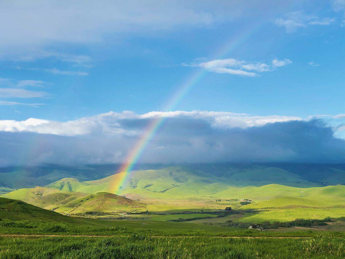 A rainbow arches over green hills near Los Osos on April 14, 2024.