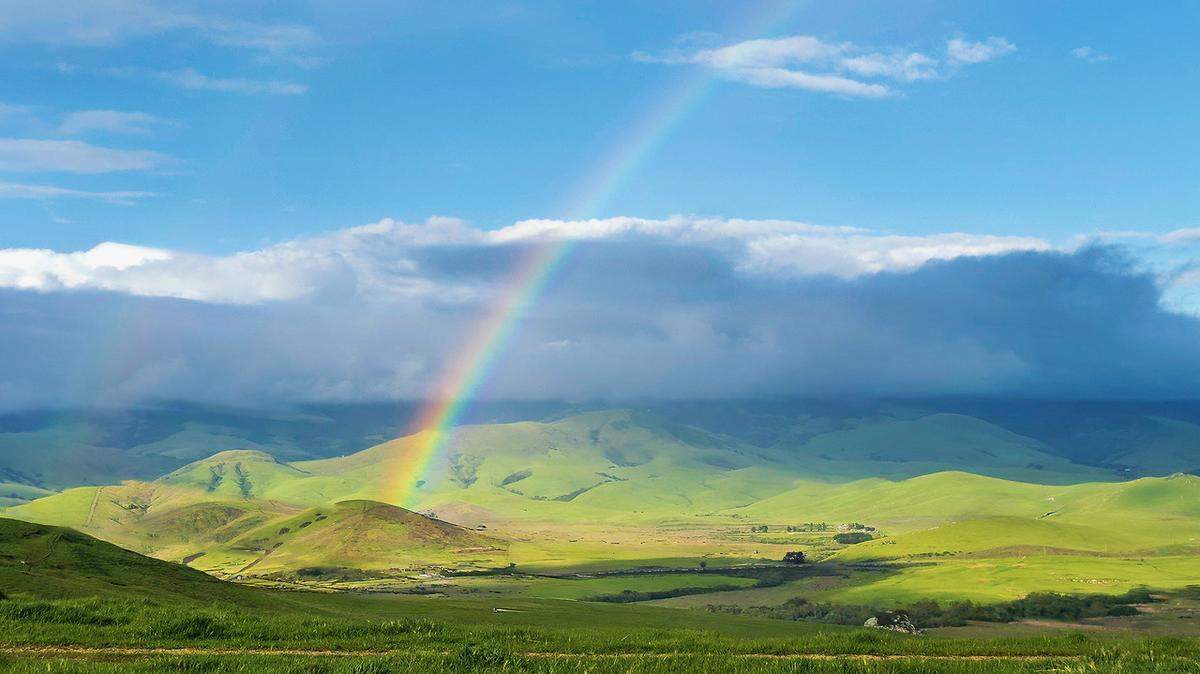 A rainbow arches over green hills near Los Osos on April 14, 2024.