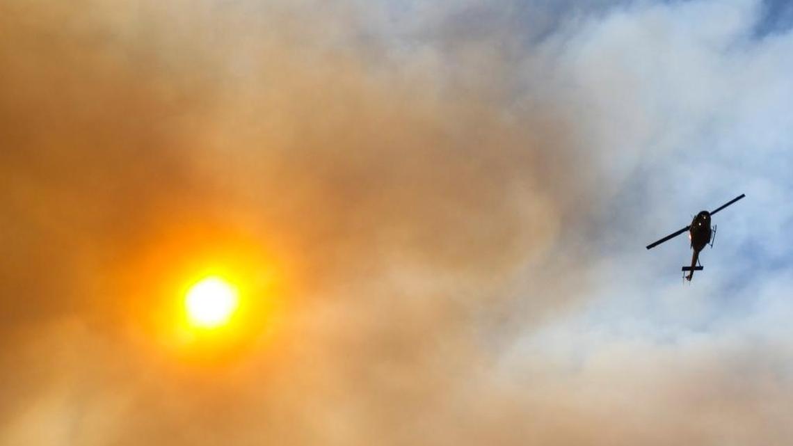 A helicopter shuttles water from Twitchell Reservoir to the Alamo Fire on Friday as smoke obscures the sun. The Alamo Fire on Highway 166 was burning south of Twitchell Reservoir Friday night and appeared to had crossed 166 to the north at another point.