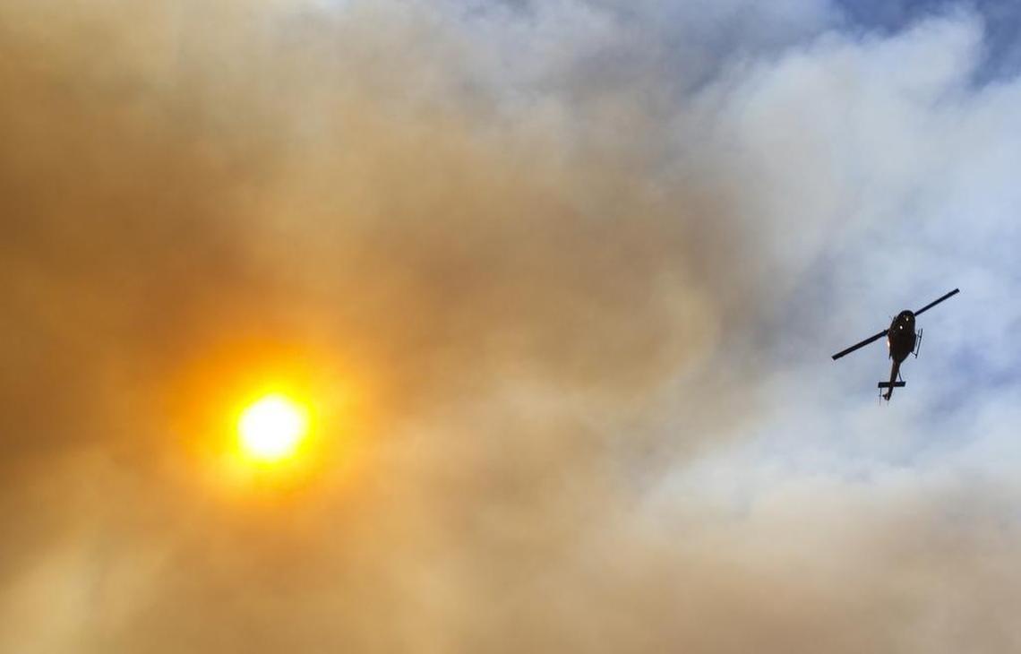 A helicopter shuttles water from Twitchell Reservoir to the Alamo Fire on Friday as smoke obscures the sun. The Alamo Fire on Highway 166 was burning south of Twitchell Reservoir Friday night and appeared to had crossed 166 to the north at another point.