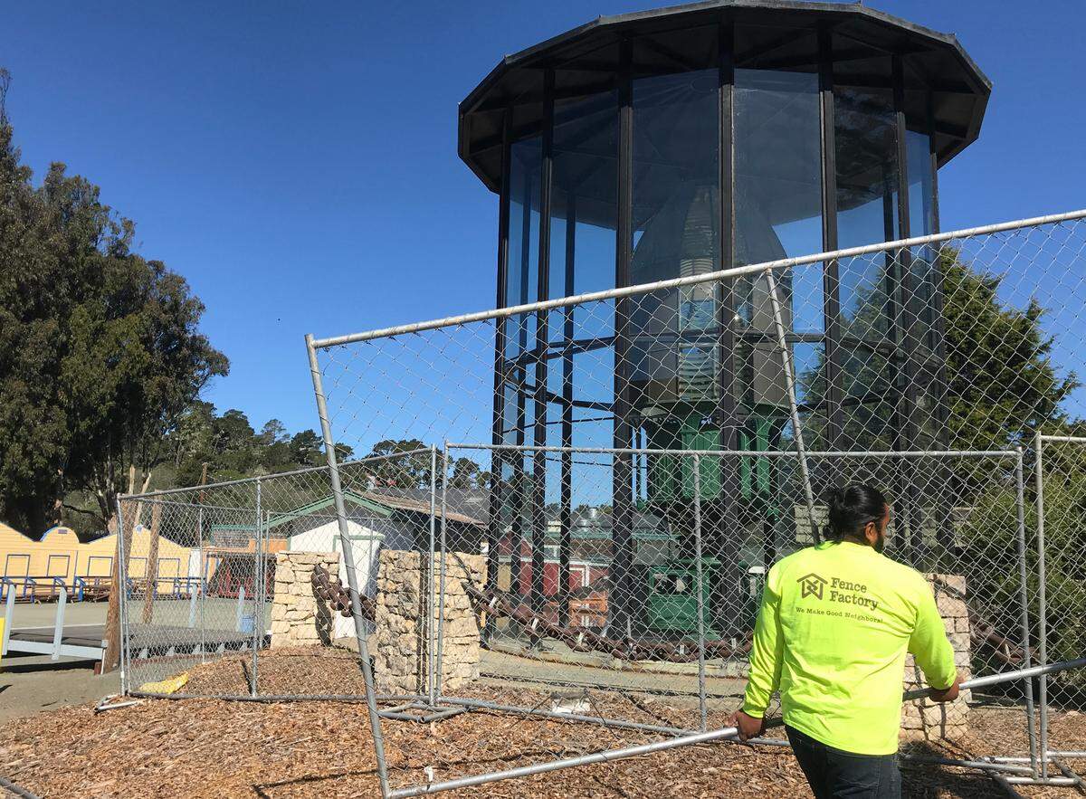 A fence installation worker carries another section of protective construction fencing to a barrier being constructed May 11, 2022, around the circa 1875 Piedras Blancas Light Station First Order Fresnel lens and its glass enclosure.