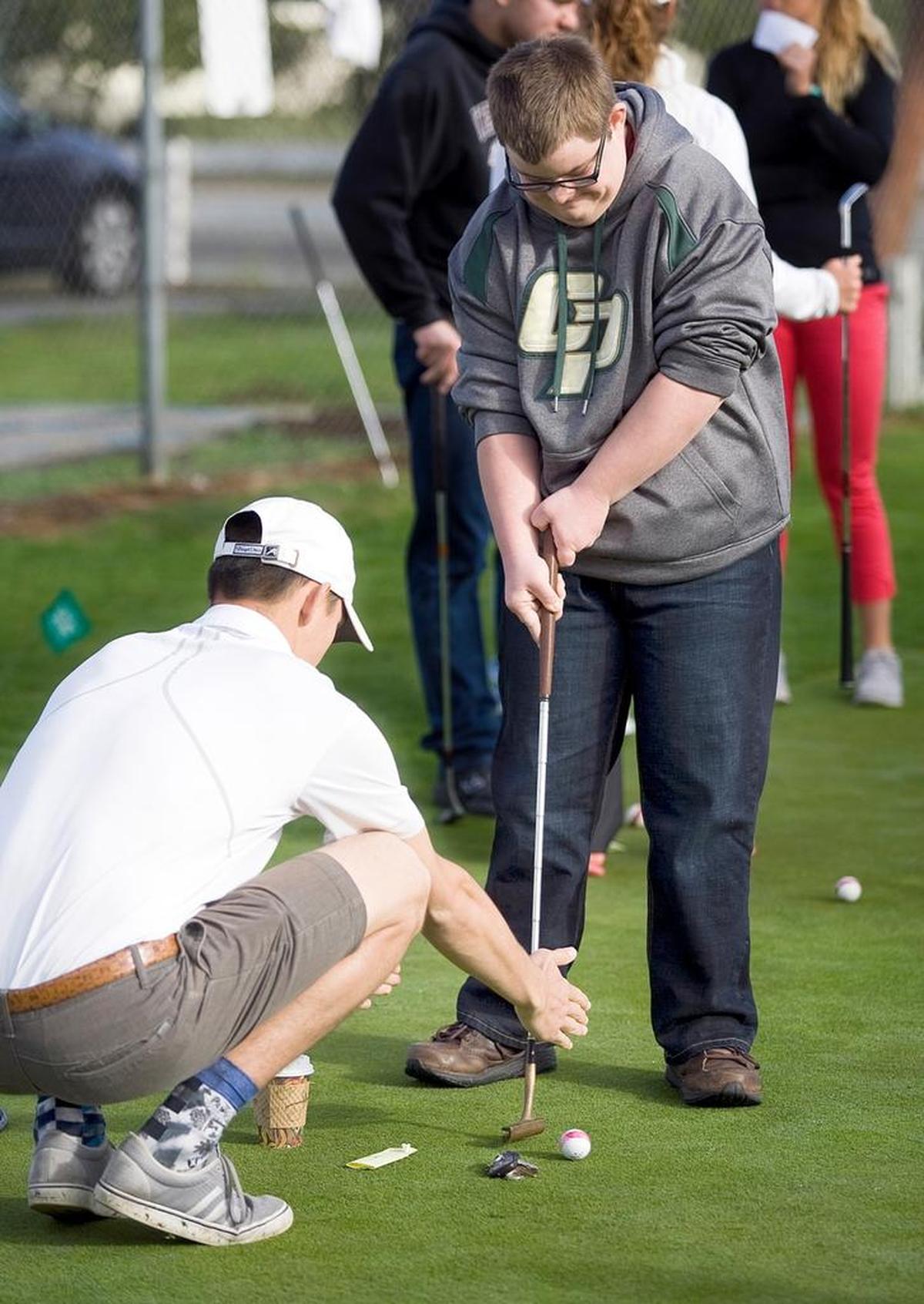 Cal Poly golf team member Mitchell Martin helps Tye Fansler, 18, of Paso Robles putt on the practice green. He used a cup and keys as markers to help Fansler measure his stroke.