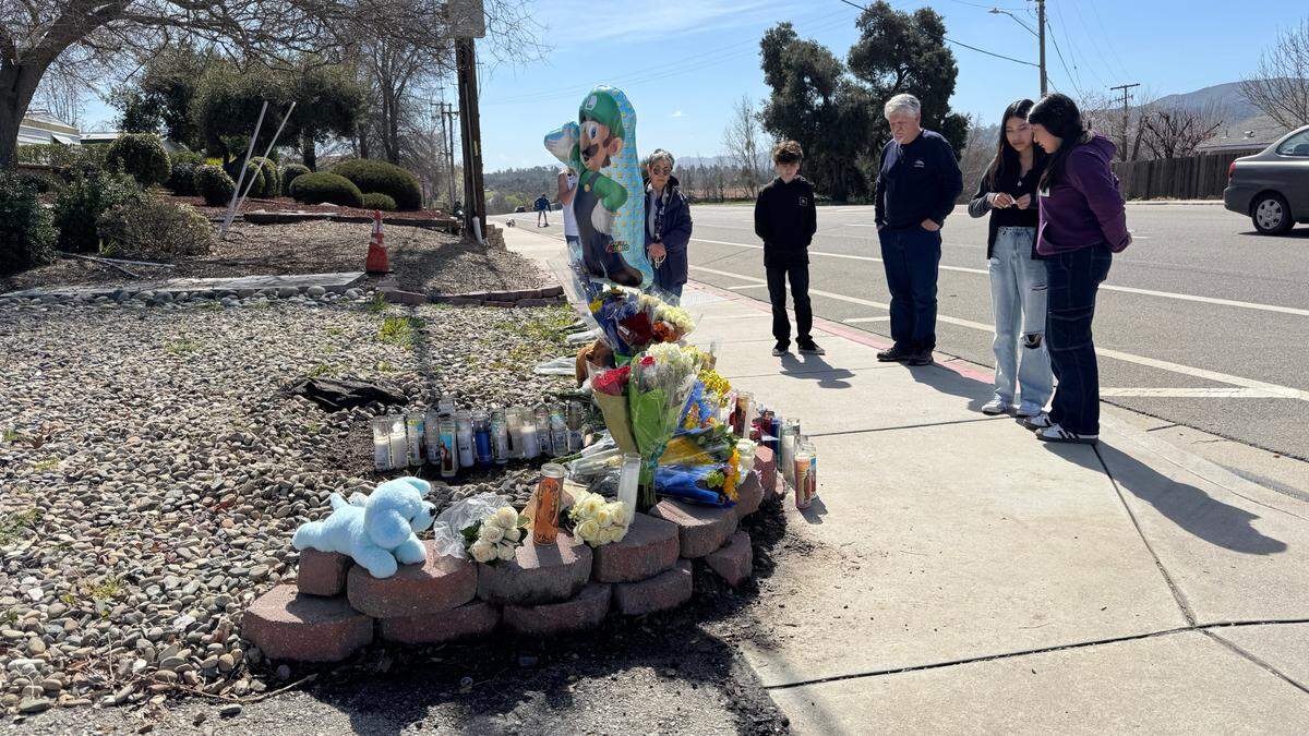 Ty Murray and his grandson Talon Doughty, center, visit a makeshift memorial along with other mourners on Saturday, March 15, 2025, for an 11-year-old Atascadero boy who was killed the day before in a hit-and-run near the Danish Care Center on El Camino Real. A gray pickup truck hit the boy on the sidewalk and then drove off.