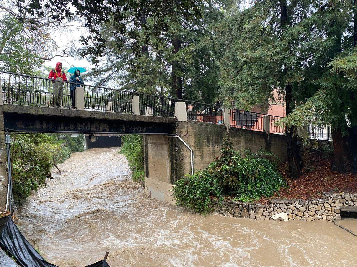 Two people watch a rushing San Luis Obispo Creek downtown on Jan. 9, 2023.