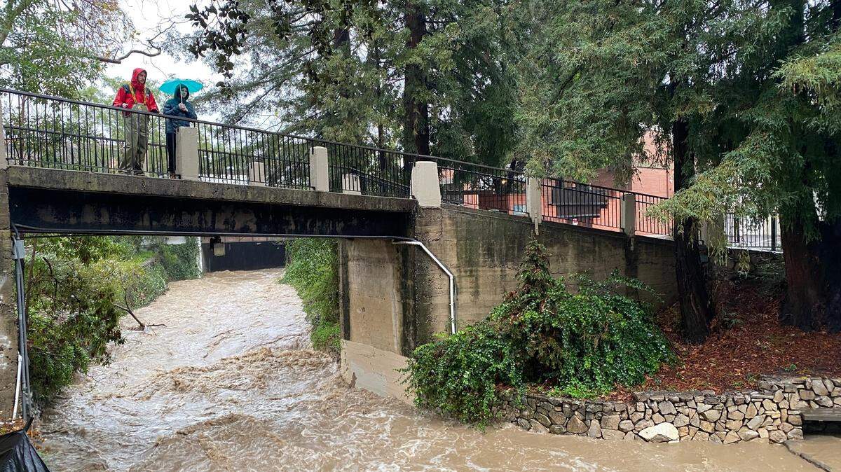 Two people watch a rushing San Luis Obispo Creek downtown on Jan. 9, 2023.