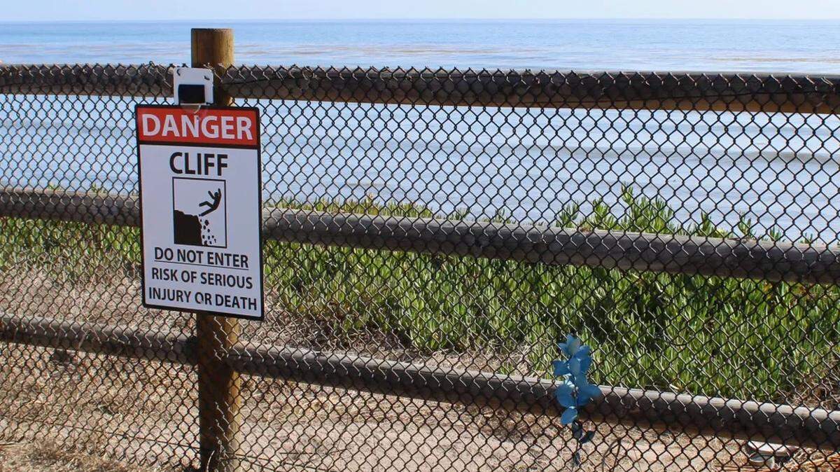 A sign warns people of the cliffs on the other side of fencing along the Isla Vista bluffs. 