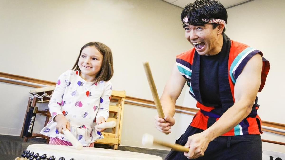 Tetsuo Uyeda, right, helps give a drumming lesson to Maggie Scozzari, 6, as part of a performance by Ichimi Daiko at the Atascadero Library. The San Luis Obispo taiko band performs Saturday at the Los Osos Library.