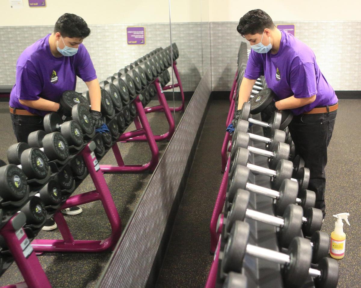 Kayla Duran cleans free weights next to the mirrored wall at Planet Fitness in Arroyo Grande. Cleaning equipment is part of the protocol with reopening.