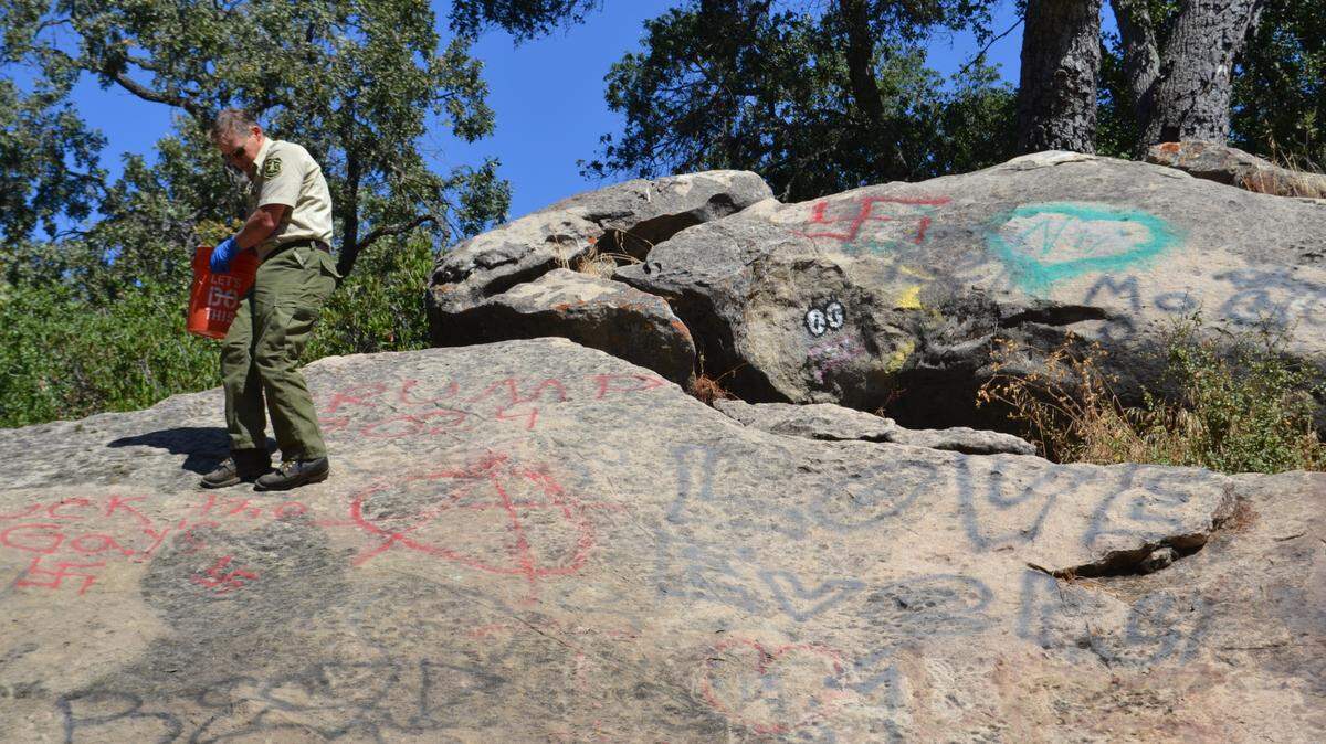 Los Padres National Forest fire service spokesperson Flemming Bertelsen prepares to scrub graffiti off of a rock formation on Wednesday, Sept. 27, 2023. 