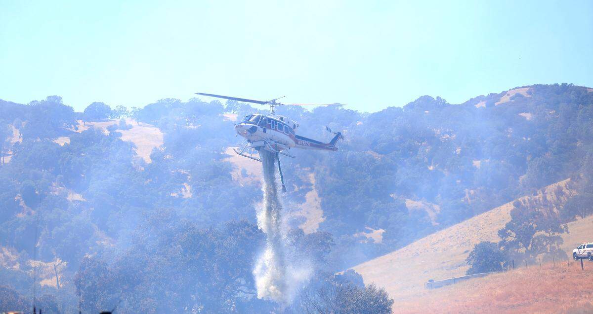 A helicopter dumps water on a vegetation fire that burned 54 acres near Highway 101 just south of Atascadero.