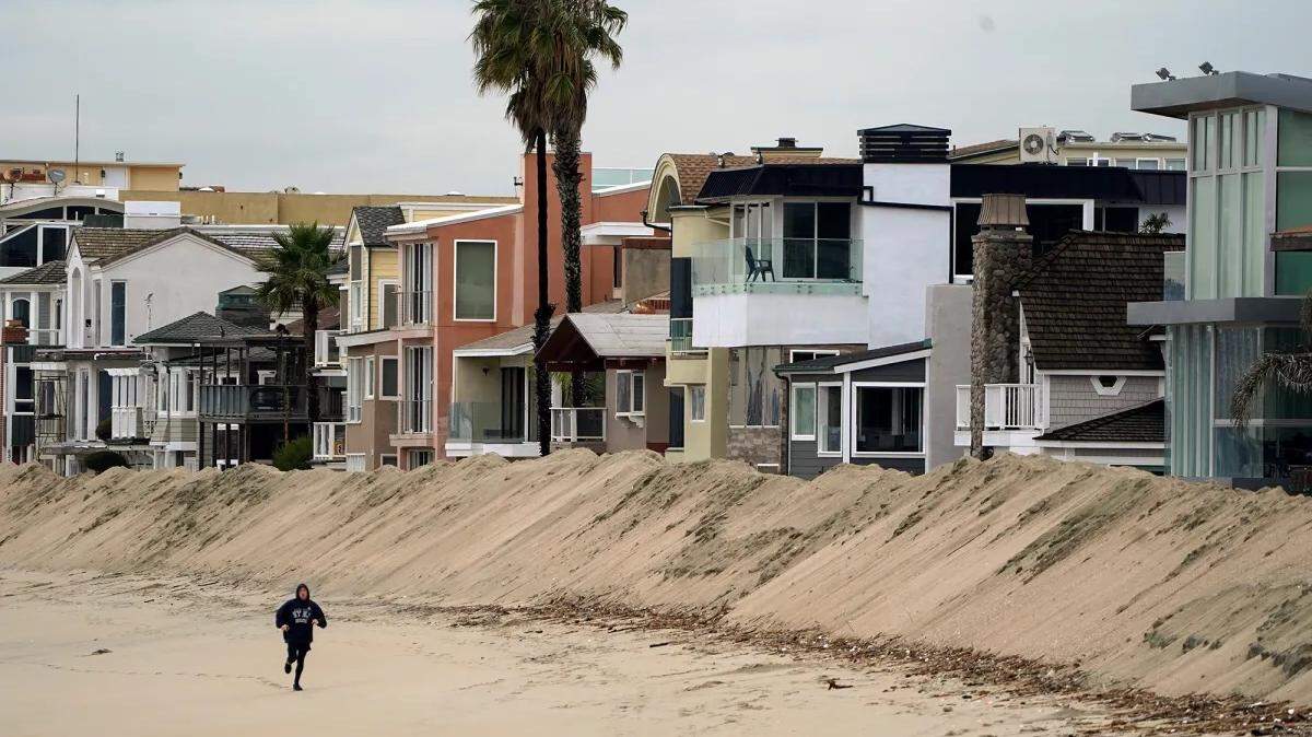 A jogger runs past a large sand berm built to protect low-lying homes from winter storms along the Peninsula neighborhood of Long Beach on Dec. 23, 2019.