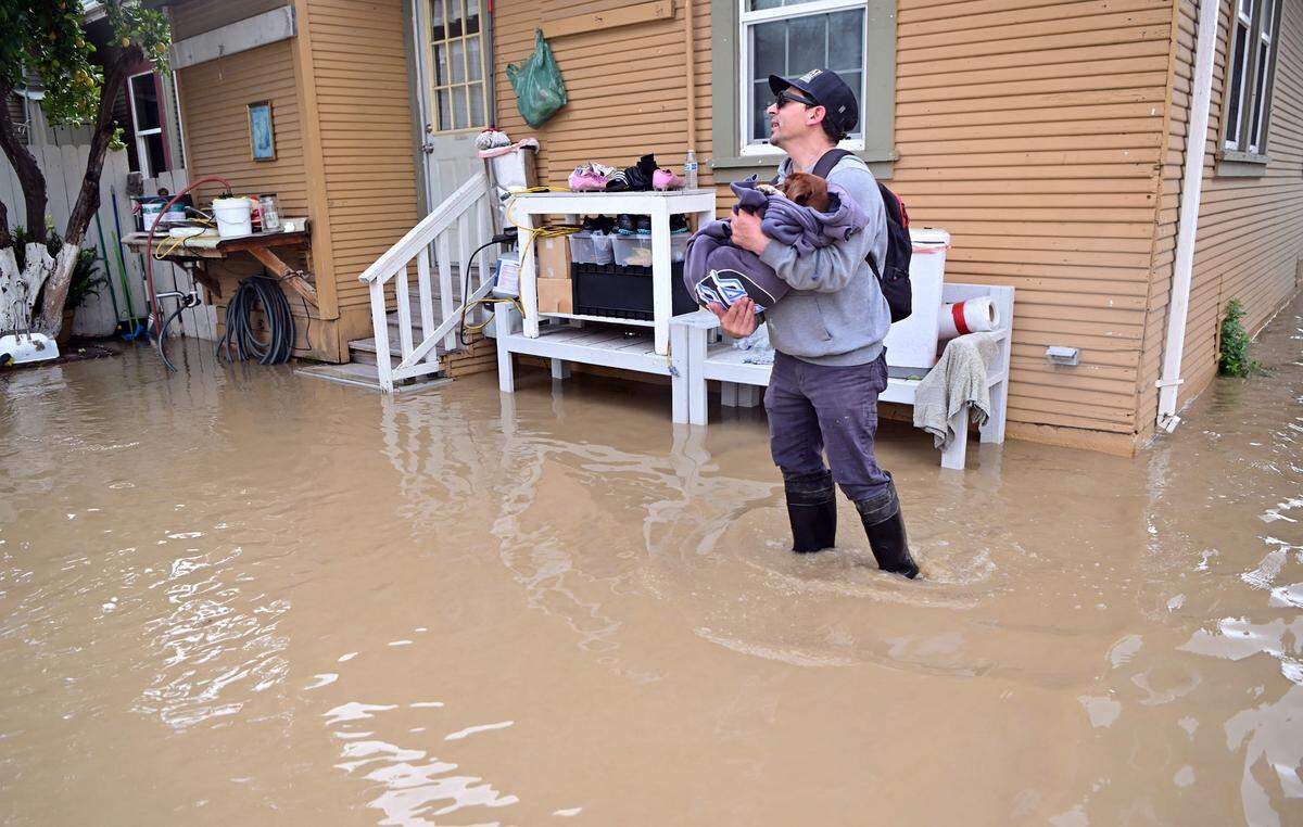 Miguel Sepulveda carries his dog from his flooded home in the Pajaro area of Watsonville, California on Saturday, March 11, 2023. Residents were forced to evacuate in the middle of the night after an atmospheric river surge broke the the Pajaro Levee and sent flood waters flowing into the community. 