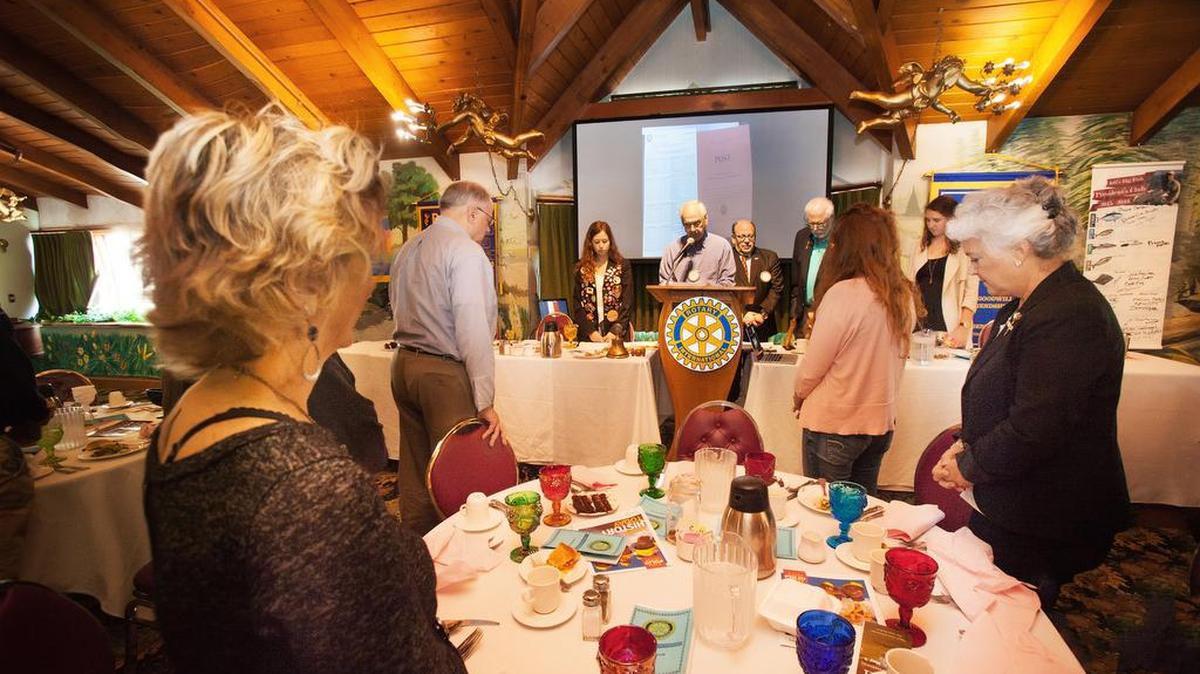 Charline Doyen, a San Luis Obispo High School senior from Namura, Belgium, left of the podium, listens as Dale Wolff leads the invocation. Also at the head table from right of Wolff are Jeff Stulberg, club president, Jim Lewis and Amber Bjerre, SLOHS Interact vice president.