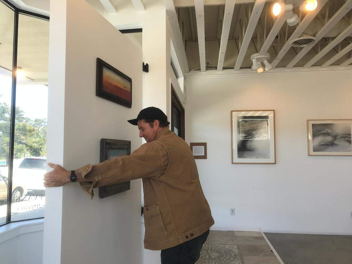 Charlie Smith, owner of Cambria’s new Cruise Control Gallery, swings a moveable wall section into place to block the view of parked vehicles and traffic in front of the gallery. At sunset, he moves the barrier out into the room, so the golden light can stream into the shop.