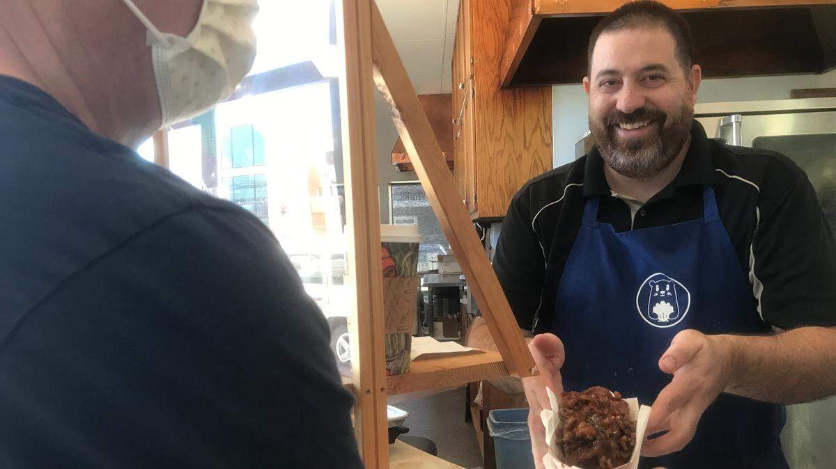 David Montemayor of Blue Shell’s Sweets & Treats hands a customer one of the the shop’s most popular products, a freshly baked, cinnamon roll.