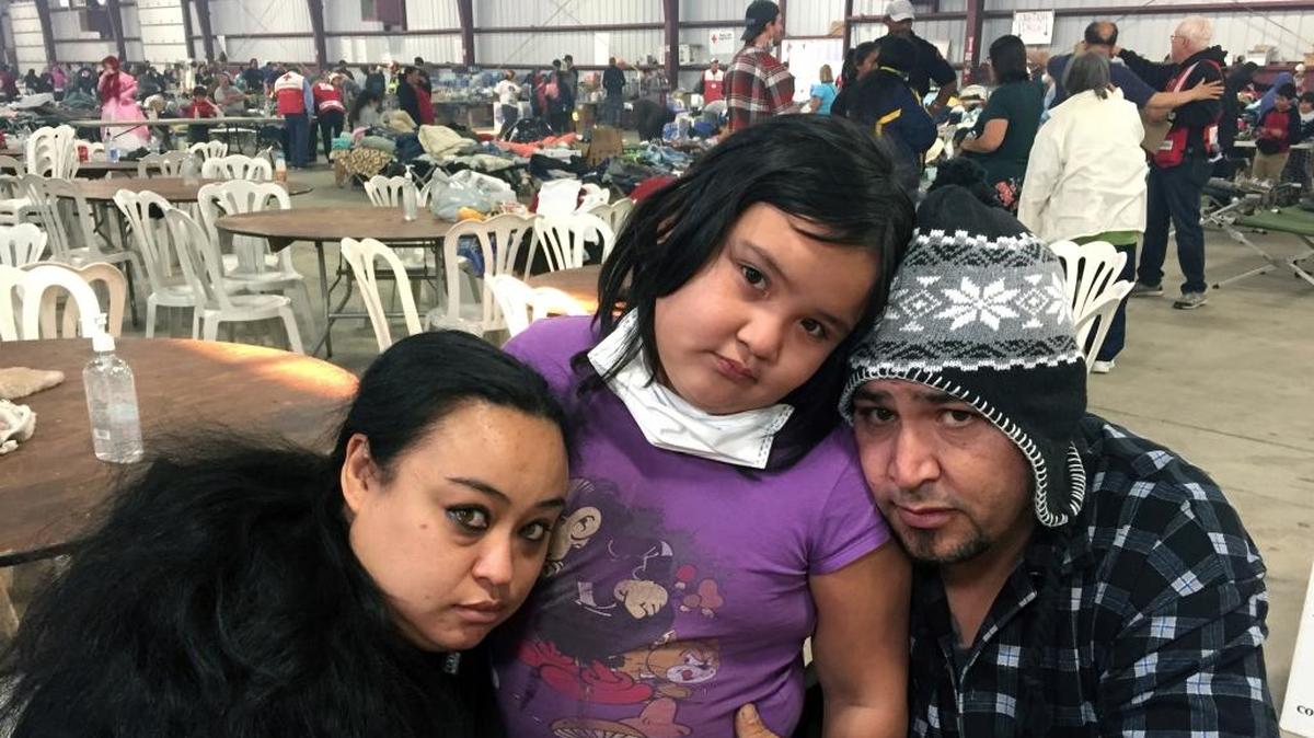 Thomas Fire survivors Marolyn Romero-Sim and Hugo Romero-Rodriguez, with their 9-year-old daughter, Milagros, sit inside the evacuation center at the Ventura County Fairgrounds on Dec. 6. The family watched their home of four years, an RV, burn in the wildfire. A donation by Community West Bank aims to help Thomas Fire victims.