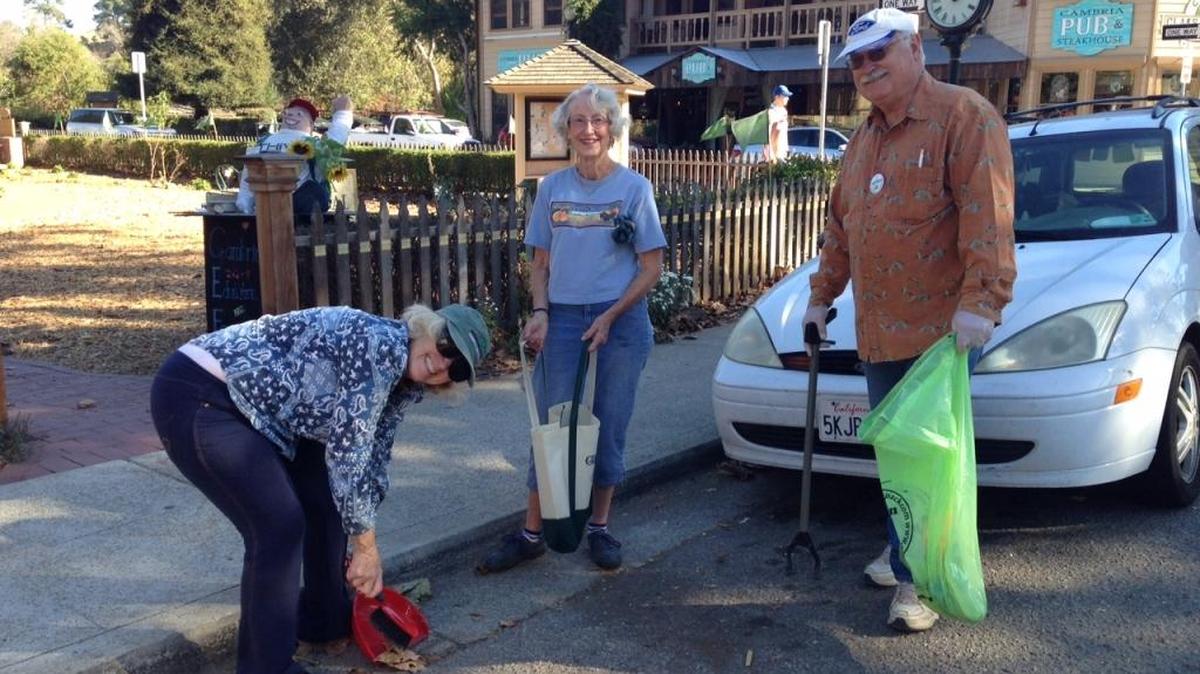 Christine Heinrichs sweeps the gutter as Marj Sewall stands by with her stewardship bag and Gordon Heinrichs uses a grabber for those hard-to-reach bits of trash at a past Squibbing Day in Cambria.