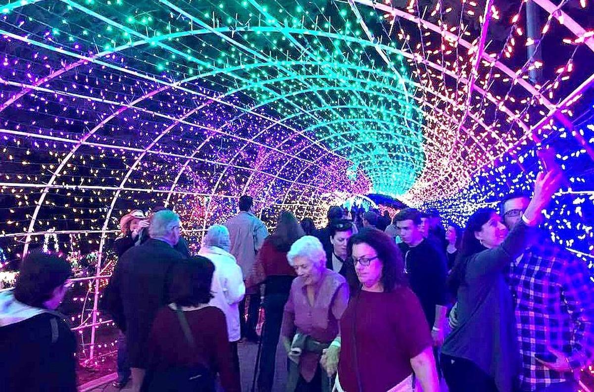 A couple, right, stops to take a selfie amid throngs of visitors in the lighted tunnel entrance to the display area at the Cambria Christmas Market on opening night, Friday, Nov. 24.