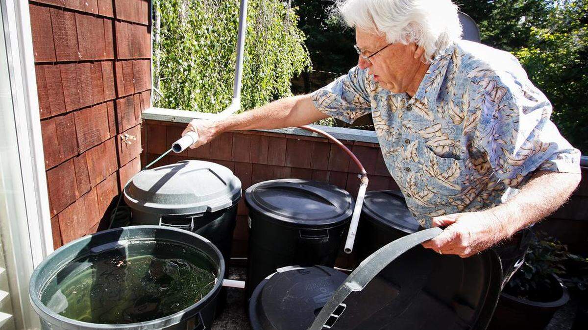 Bill Seavey of Cambria with one of his homemade rainwater catchment systems. The pipe he's holding is connected to the house's rain gutter and swivels so it can fill up any of these 32-gallon garbage cans.