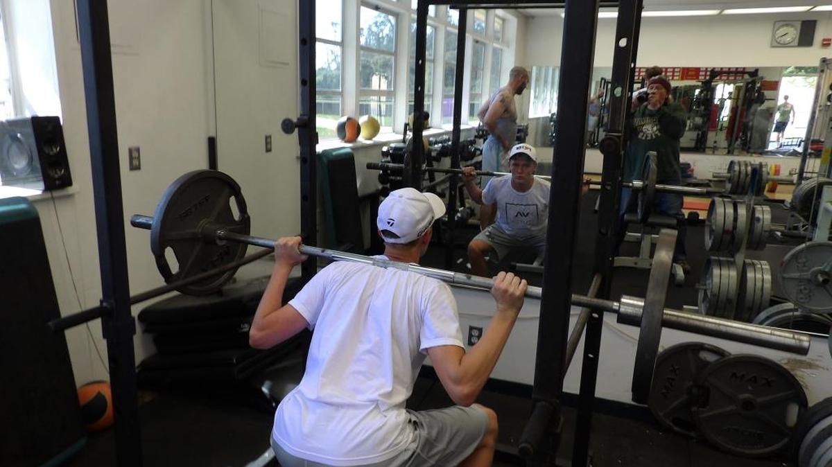 Senior basketball player Nick Roper performs squats in the Coast Union weight room Monday, June 20. Coach Tim May, background, supervises the volunteer workouts.