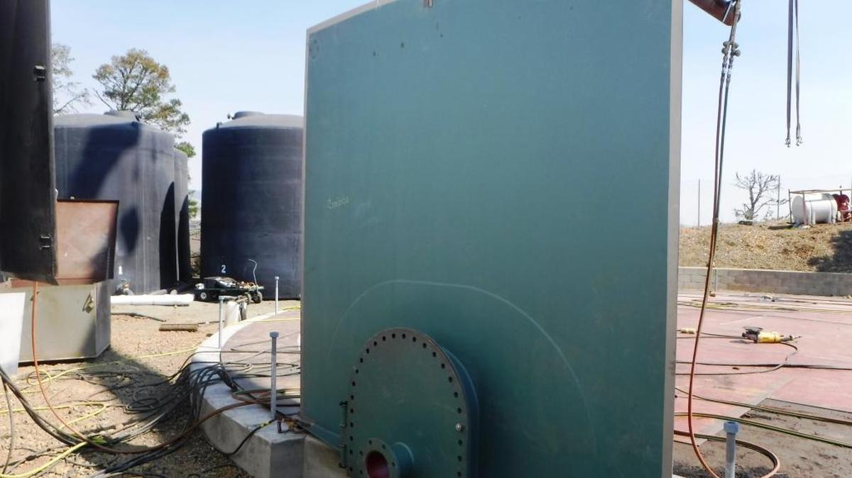 The about-to-be-installed first side-wall piece of the new Fiscalini Water Tank is seen Tuesday, Sept. 27. The temporary tanks (black) are in the background to the left, and one of the emergency water-supply-and-pump combinations for firefighting is shown at the right on the cleared-off fire-buffer zone.