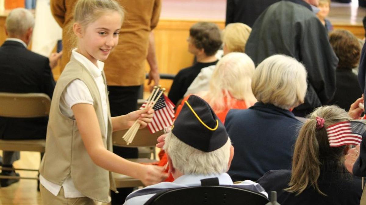 Lisi Happel, representing the Girl Scouts, hands a miniature American flag to a veteran at the Nov. 11 commemoration. Lisa also recited a poem titled “Veterans Day.”