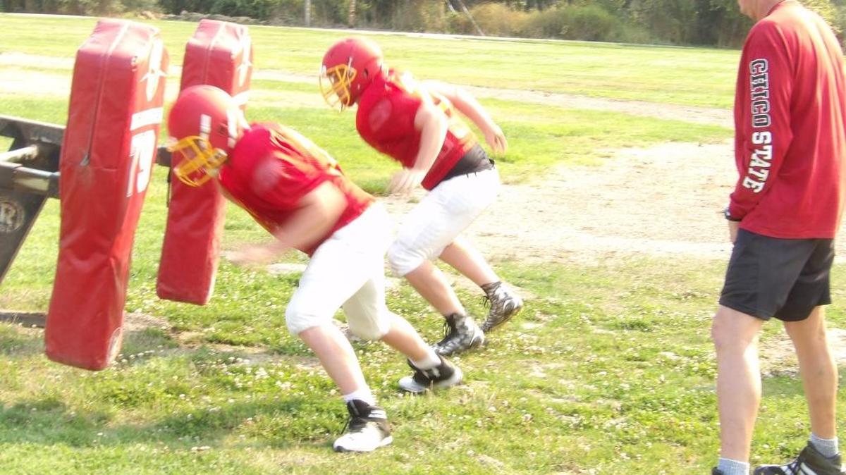 Freshman center Spencer Magnuson, left, and sophomore lineman Gary Lyons attack the blocking dummies during practice Wednesday, Aug. 17, with assistant coach Marty Maples supervising.