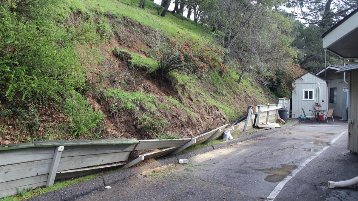 A mudslide buckles a wooden fence Monday morning behind the Cambria Community Healthcare District ambulance station on Main Street in the community’s East Village.