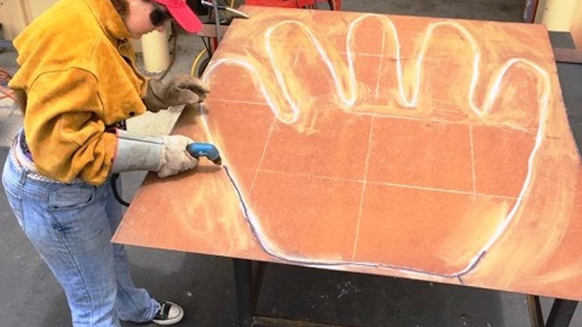 Coast Union freshman Melody Robertson works with a plasma cutter to cut a graphed-out shape.