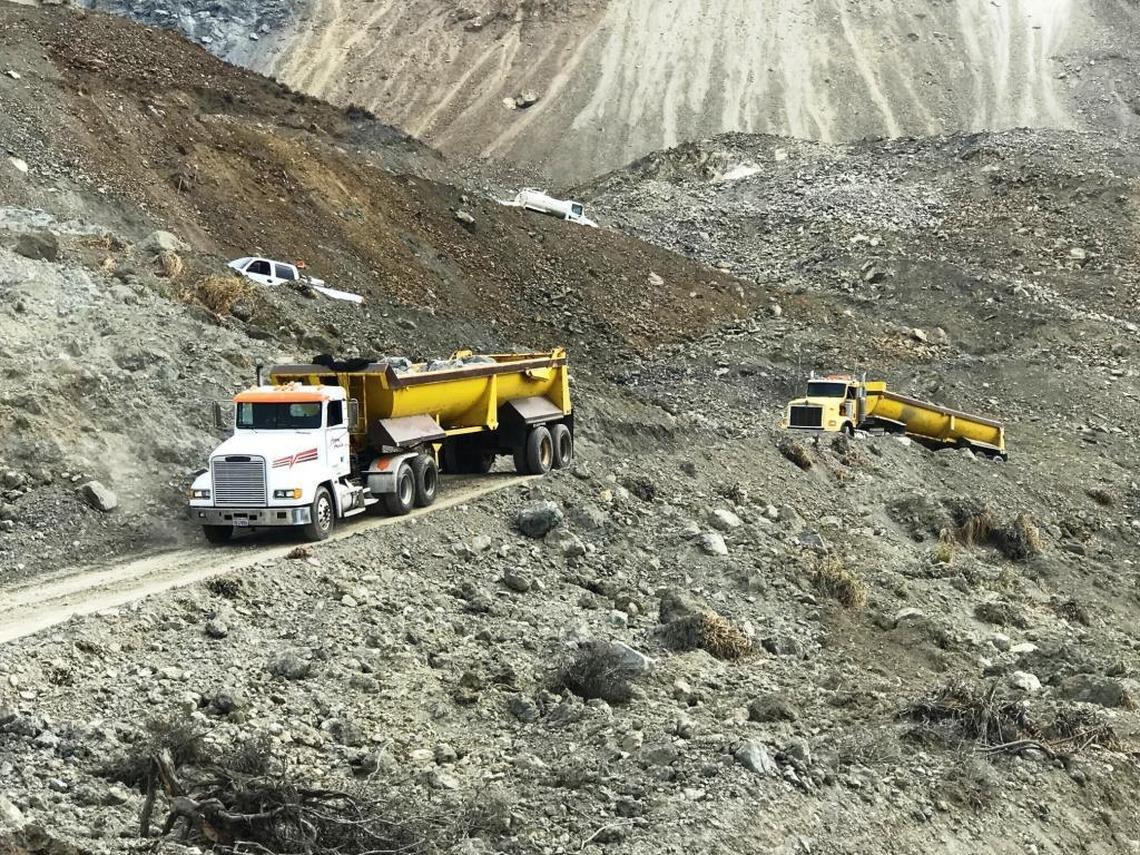 Big rigs haul boulders along a temporary road at the Mud Creek slide early this month.