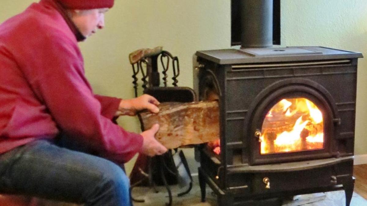 The columnist’s husband, John, builds a fire in their wood-burning stove, their home’s source of heat in winter.