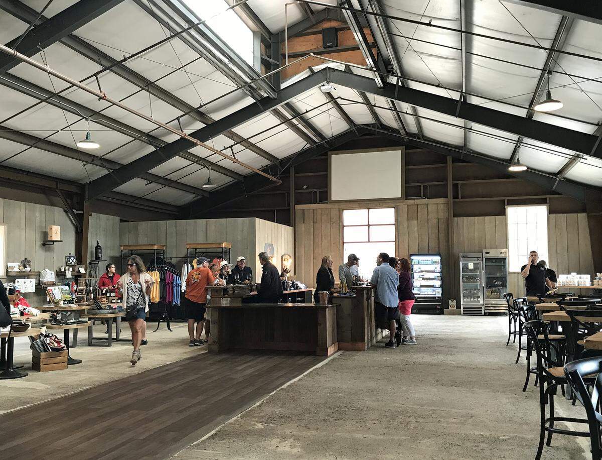 A former warehouse, the new Hearst Ranch Winery tasting room has a rustic but upscale industrial look, with a soaring ceiling, black metal beams, skylights concrete floor with a wood runway and wine bar.
