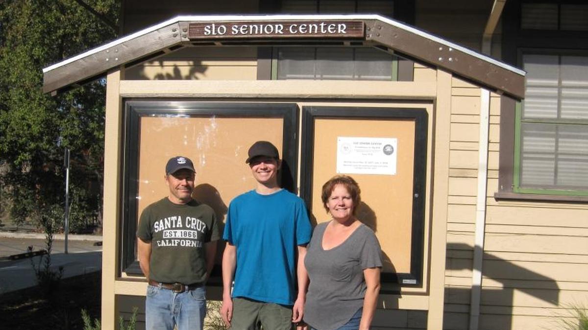 Jason Dixon, with parents Dan and Lori, stands in front of his Eagle Scout project — an outdoor message board at the San Luis Obispo Senior Center.