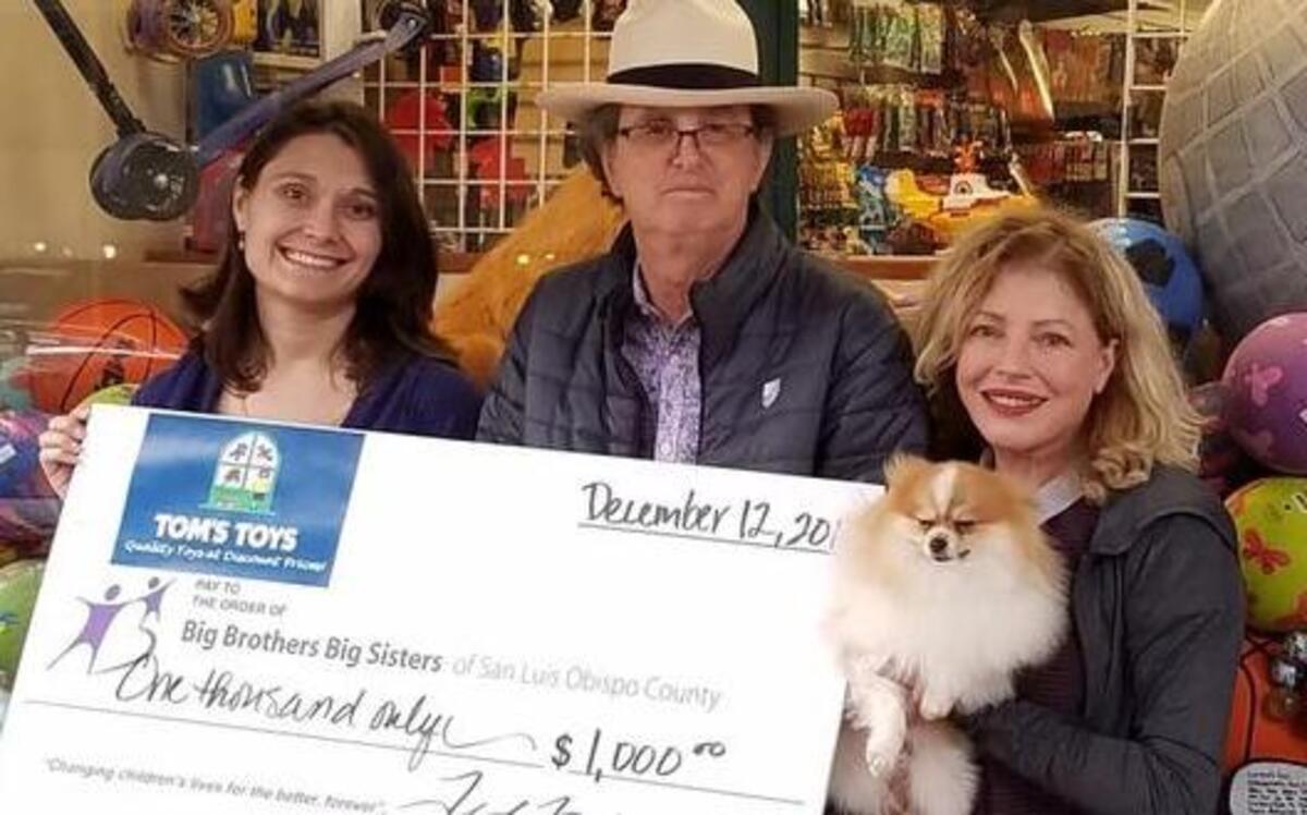 From left, Big Brothers Big Sisters Executive Director Anna Boyd-Bucy receives a donation from Tom’s Toys owners Ted and Anne Frankel (holding their dog, Rocky).