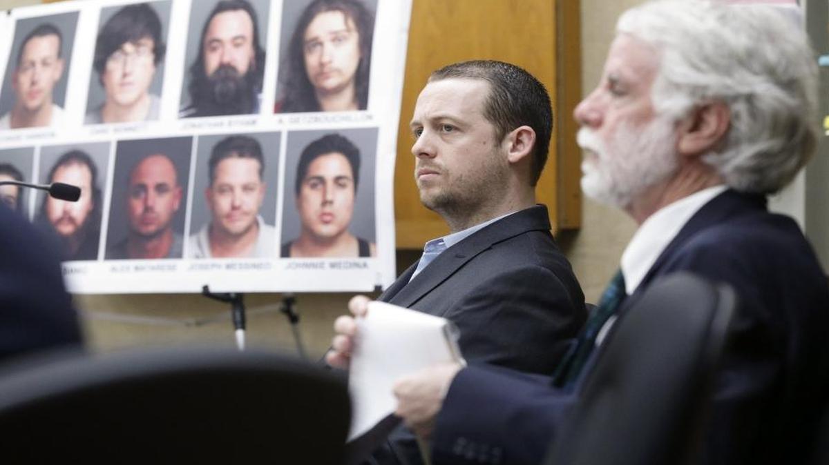 Chase Hanson, center, is accused of being the leader of a drug ring that sold cocaine and other substances. His attorney Jeffry Radding is seated at right. In the background are faces and names of those implicated in the investigation.