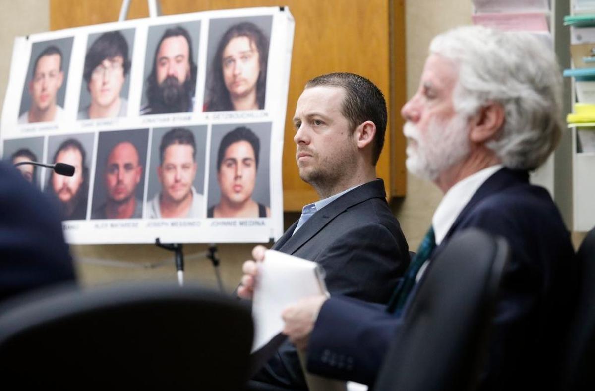 Chase Hanson is accused of being the leader of a drug ring that sold cocaine and other substances. His attorney Jeffry Radding is seated at right. In the background are faces and names of those implicated in this investigation.