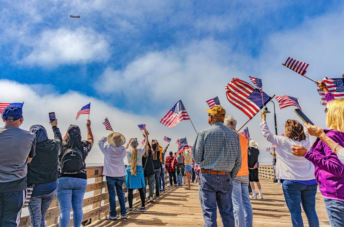 Supporters wave American flags on the Cayucos Pier as the C-47 Betsy’s Biscuit Bomber flies overhead on Saturday, Aug. 28, 2022, during an Honor Flight from Paso Robles to the coast for 17 veterans.