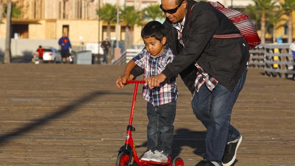 Juan Valencia of Pismo Beach helps stepson JoJo, 3, with scootering on the uneven planks of the Pismo Pier.