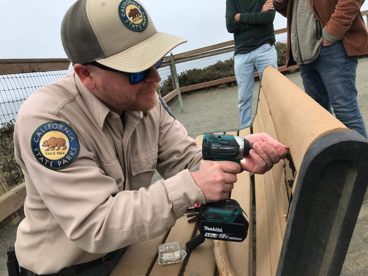 California State Parks employee Evan Feeney installs memorial plaques on July 11, 2022, on a bench honoring Richard Tanner, late husband of Tribune columnist Kathe Tanner. The bench overlooks the elephant seals at the rookery south of Piedras Blancas.