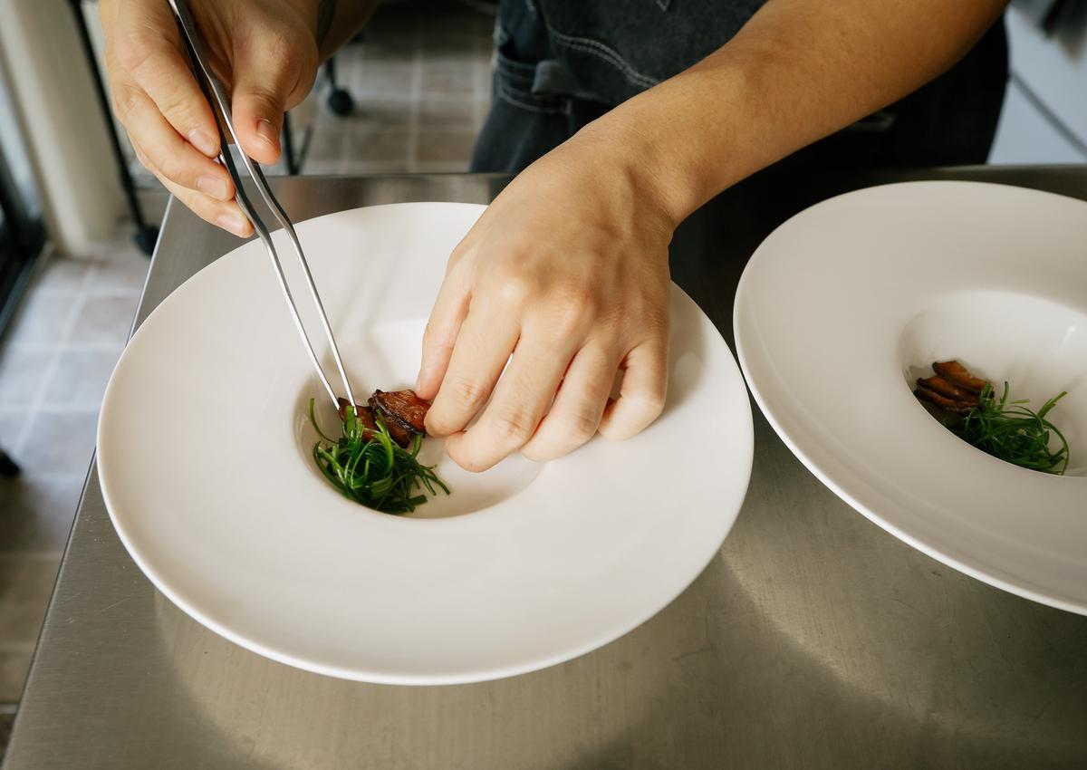 Cal Poly student Jimmy Wong arranges sliced scallions and sauteed trumpet mushrooms in a bowl. He runs a pop-up restaurant, Dench, out of his studio apartment in San Luis Obispo.