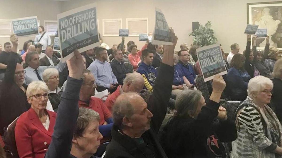 Members of the crowd hold up signs opposing offshore oil during Wednesday’s Coastal Commission meeting in Cambria.