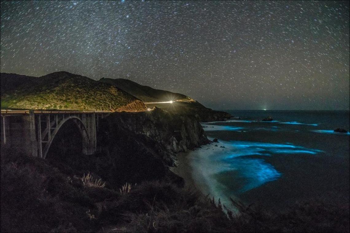 Glowing blue waves, caused by bioluminescent dinoflagellates, create a mesmerizing scene near the Bixby Creek Bridge in Big Sur.