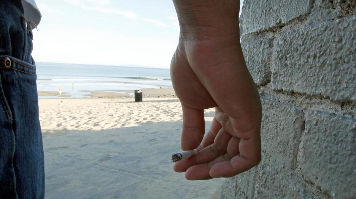 Ian Zamora holds his cigarette at the wall separating the parking area from the sand at Surfrider Beach in Malibu. A hashtag campaign aims to convince the governor to ban smoking at California beaches.