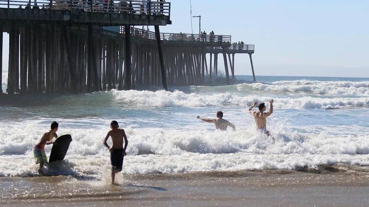 People splash in the waves next to the Pismo Beach Pier.