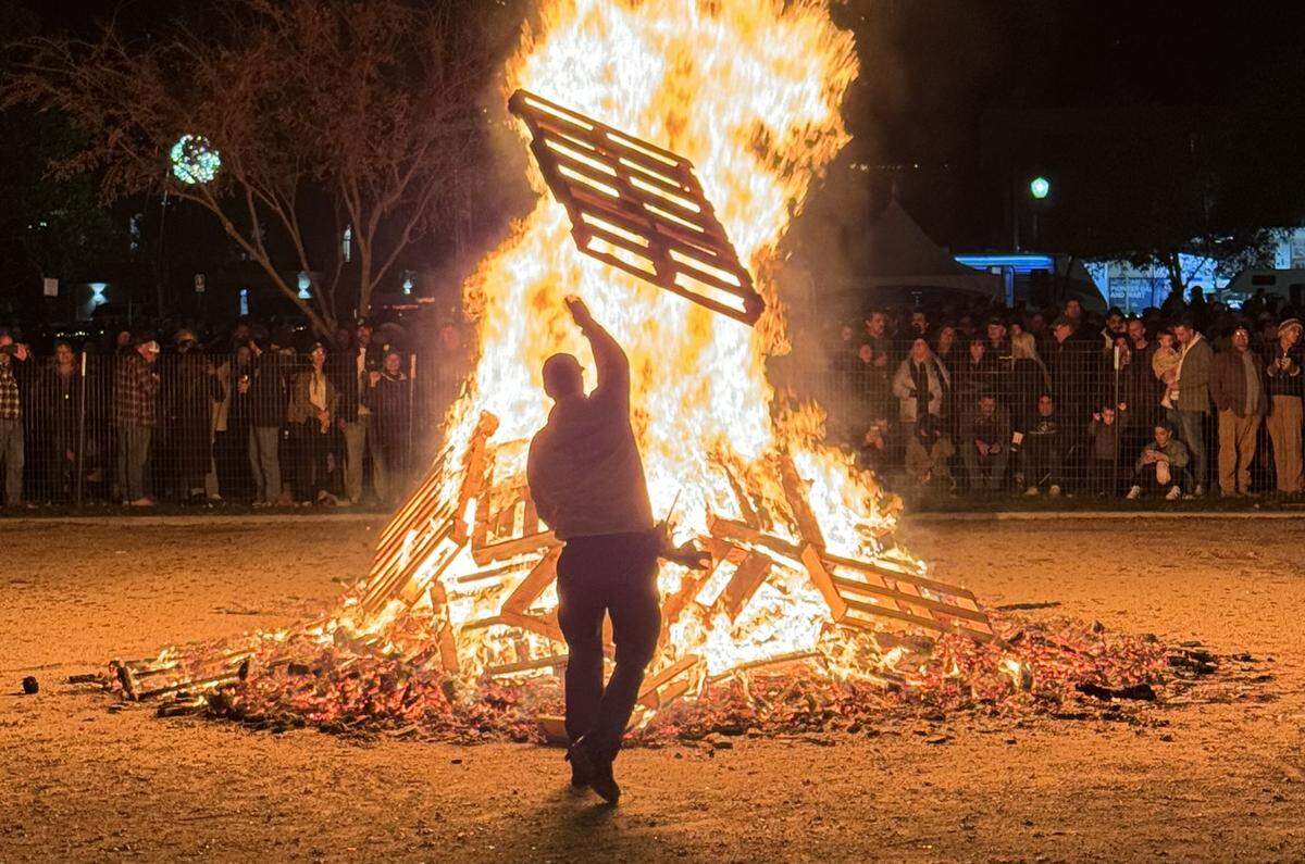 A firefighter throws a pallet onto the giant bonfire at Paso Robles’ New Year’s Eve celebration in the Downtown City Park on Dec. 31, 2023.